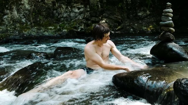 Man bathes in a mountain river among stones and a cairn