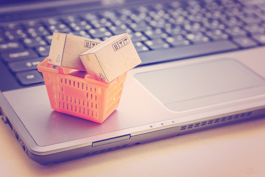 Online shopping / retail ecommerce and delivery service concept : Small boxes in an orange shopping basket on a laptop, depicts consumers purchase or order products from suppliers or digital stores.
