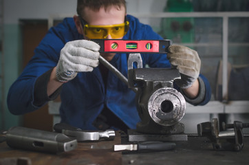 Man worker is working with iron detail on vise grip on blacksmith table.