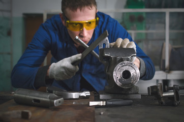 Man worker is working with iron detail on vise grip on blacksmith table and using a file.