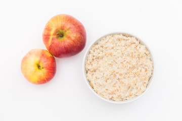 Oatmeal in white bowl and red apple on white background. Isolated on white. Healthy food