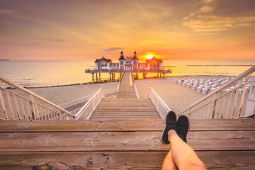 Papier Peint photo autocollant Jetée Young man sitting on wooden pier enjoying sunrise at Seebrucke Sellin, Baltic Sea, Germany