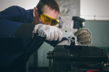 Man worker is working with iron detail on vise grip on blacksmith table and is measuring a diameter...