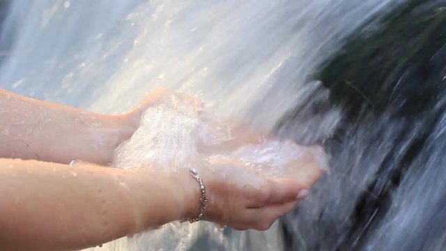 women's hands in the clear water of the waterfall