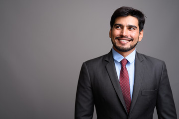 Young handsome bearded Persian businessman against gray backgrou