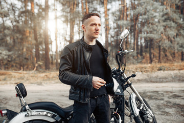 Handsome rider guy in black biker jacket on classic style cafe racer motorcycle at sunset. Bike...