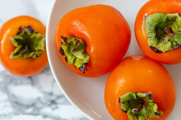 Ripe persimmons in a bowl on a white marble table