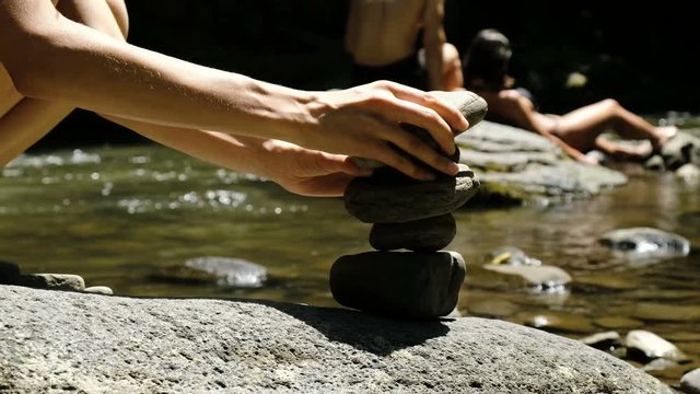 Girl puts a cairn close-up standing on a cobblestone in a mountain river against the background of tourists, the tower falls