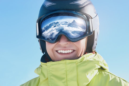 Close up of the ski goggles of a man with the reflection of snowed mountains.  A mountain range reflected in the ski mask.  Portrait of man at the ski resort.  Wearing ski glasses. Winter Sports.