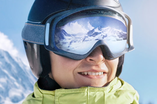 Portrait of man at the ski resort on the background of mountains and blue sky.A mountain range reflected in the ski mask