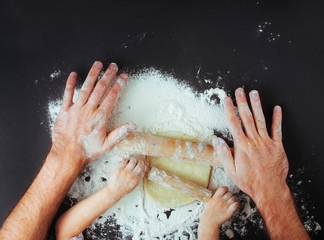 Top view of fathers and kids hands rolling the dough on black background