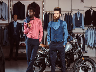 Fototapeta na wymiar Two stylish elegantly dressed men standing near retro sports motorbike at the men's clothing store.
