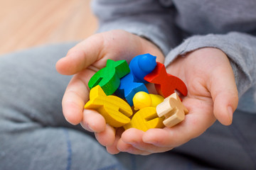little blonde girl hold red people figure in hand. yellow, blue, green wood chips in children play - Board game and kids leisure concept