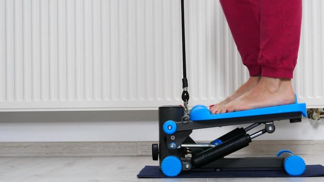 Woman doing exercises at home on stepping machine. Female legs foot on stepper trainer