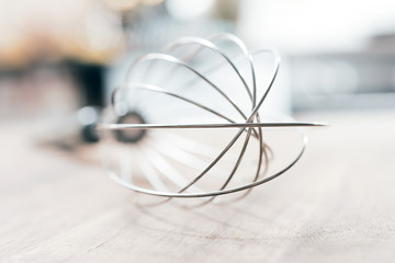 Stainless Whisk On A Wooden Table With Blurred Out Kitchen Background