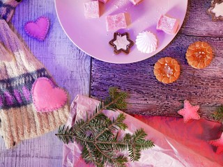 Seasonal decorative still life of sweet dessert, Christmas balls and felt toys on a wooden textural background, illuminated with blue and pink light, winter, Christmas, new year
