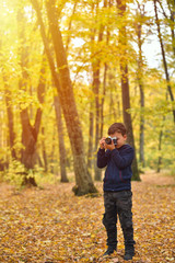 Creative child, kid photographer (a little boy) with a camera taking pictures of colorful autumn forest