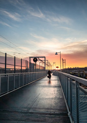 Man cycling with black jacket over a bridge in gothenburg sweden with rising sun in the pink sky