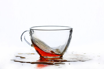 A splash of tea in a glass tea cup on a white background.