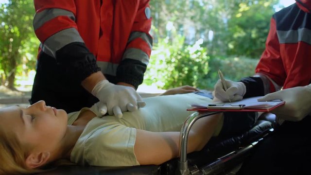 Paramedic doing CPR to girl, colleague making records, professional saving life