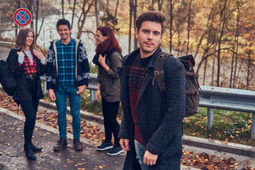 Group of young hikers standing on the road sidelines at beautiful autumn forest.