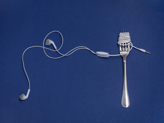 Studio shot of earphones wrapped around a fork against a blue background