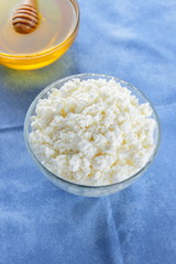 Cottage cheese. Cottage cheese and honey on blue napkin. Soft cheese in glassware. Dairy product for breakfast. Copy space
