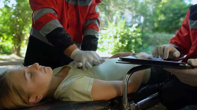 Male paramedic doing indirect heart massage, colleague using tablet for records