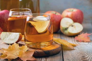 Organic Apple cider or juice on a wooden table. Two glasses with drink and autumn leaves on rustic background