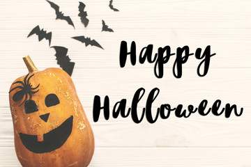 Happy Halloween text sign, flat lay. Halloween pumpkin Jack o Lantern with bats, spiders top view on white rustic wooden background. Season's greeting card