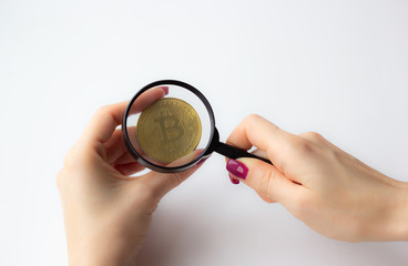 Female hand holding a magnifying glass with golden bitcoin coin on white background
