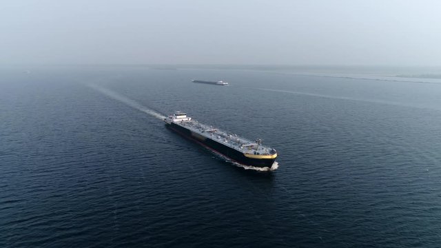 Aerial bird view footage of barge a flat-bottomed ship built mainly for river and canal transport of material goods and very heavy or bulky items this vessel travelling near coast in background 4k