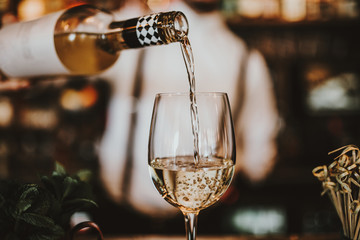 Close up shot of a bartender pouring white wine into a glass. Hospitality, beverage and wine concept.