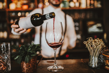 Close up shot of a bartender pouring red wine into a glass. Hospitality, beverage and wine concept. - Powered by Adobe