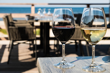 Red and white wine glasses on blurred background with served restaurant table, sea and horizon
