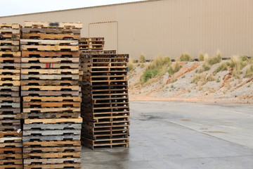 Stacks of old pallets outside a ware house. Brown wooden pallets some grey from being weathered , Old wooden cracked and damaged.