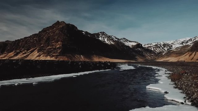 Water stream of mountain river in Iceland, is running between mountains covered in fresh snow. Late evening