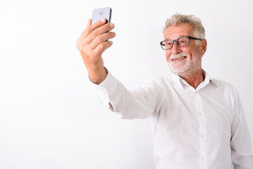 Studio shot of happy senior bearded man smiling while taking sel
