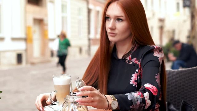 Young woman adding sugar into coffee and mixing sitting in cafe in the city , 4K
