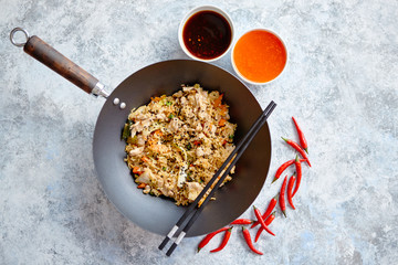 Delicious fried rice with chicken. Prepared and served in a wok with soy and sweet sour souces on side. Placed on stone background. Top view.