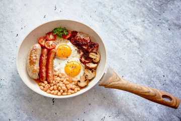 British Full English Breakfast including sausages, grilled tomatoes, mushrooms, eggs, bacon, baked beans and bread. Top view.