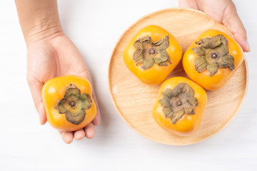 Ripe persimmon fruit on wooden plate holding by hand, top view