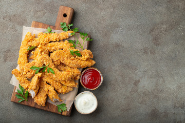Breaded chicken strips with two kinds of sauces on a wooden Board. Fast food on dark brown...