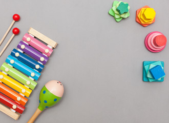 Children's toys: wooden multicolored pyramids, musical instruments maracas and xylophone on a gray background with a place for text. Flat lay, top view