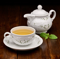 Green tea in porcelain cup and teapot with mint on wooden table 