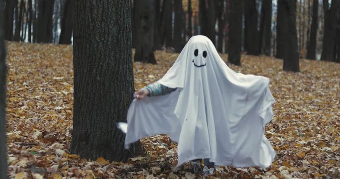 Little girl in a costume ghost with orange pumpkin. Halloween celebration holiday. Funny smiling grimace