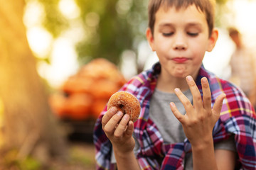 boy eating apple donut on the farm. the child holds cider donut and licks fingers. Selective focus. Blurred background, copy space for your text
