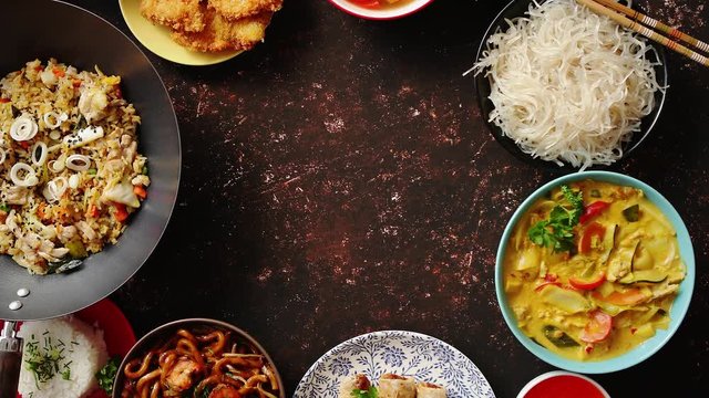 Asian food set. Noodles, fried rice with chicken, tom yum soup, spring rolls, deep fried fish and udon with prawns. Top view on dark rustic background. Oriental style food circle composition.