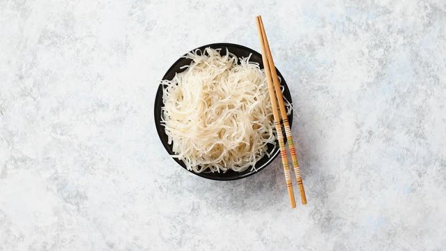 Close up of bowl of noodles with wooden chopsticks on stone table