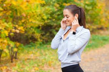 Photo of Joyful Fitness Woman 30s in Sportswear Touching Bluetooth Earpod and Holding Mobile Phone,...